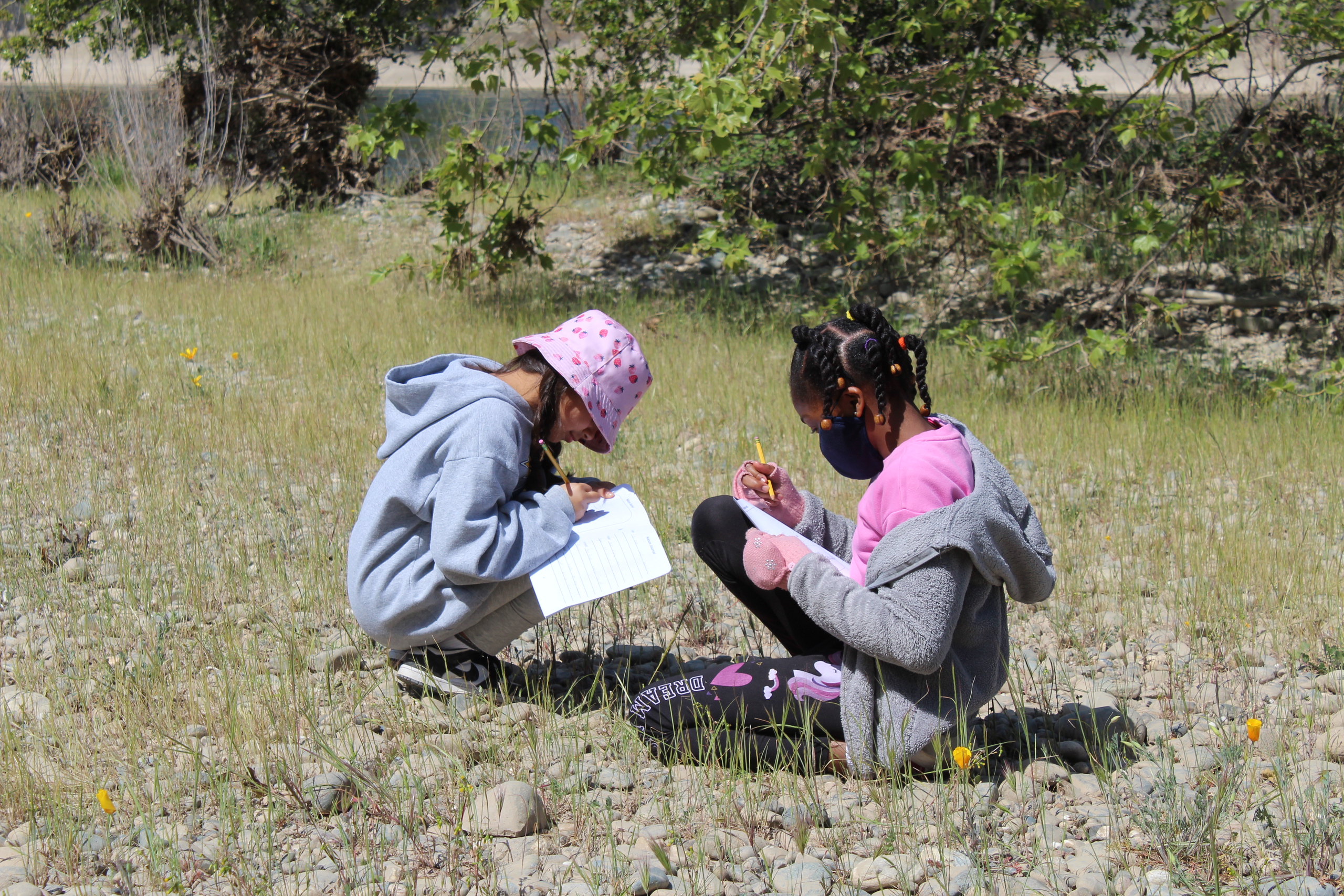 Two kids sit in a field writing in notebooks